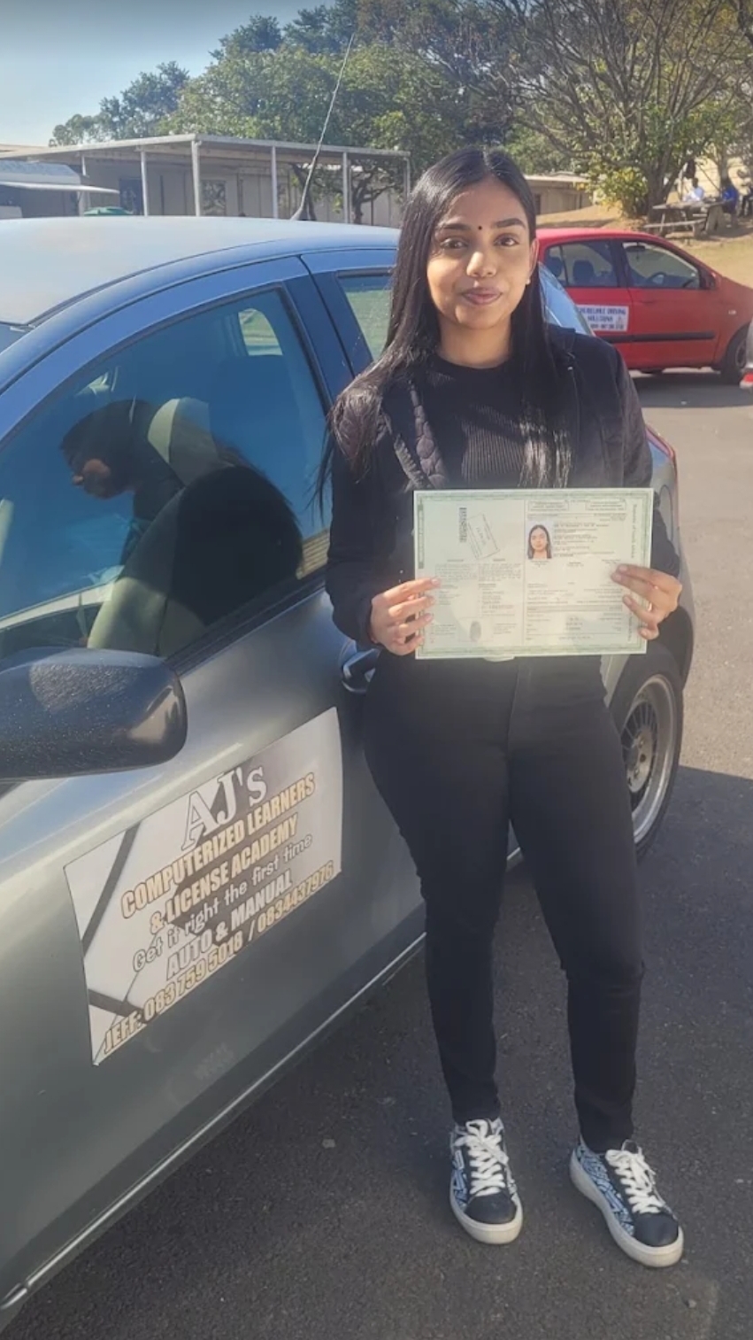 A happy student holding her learner's licence next to an AJ's Academy vehicle