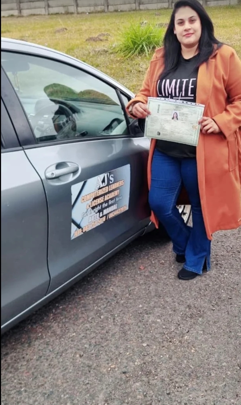 Happy student with her licence beside the branded academy car